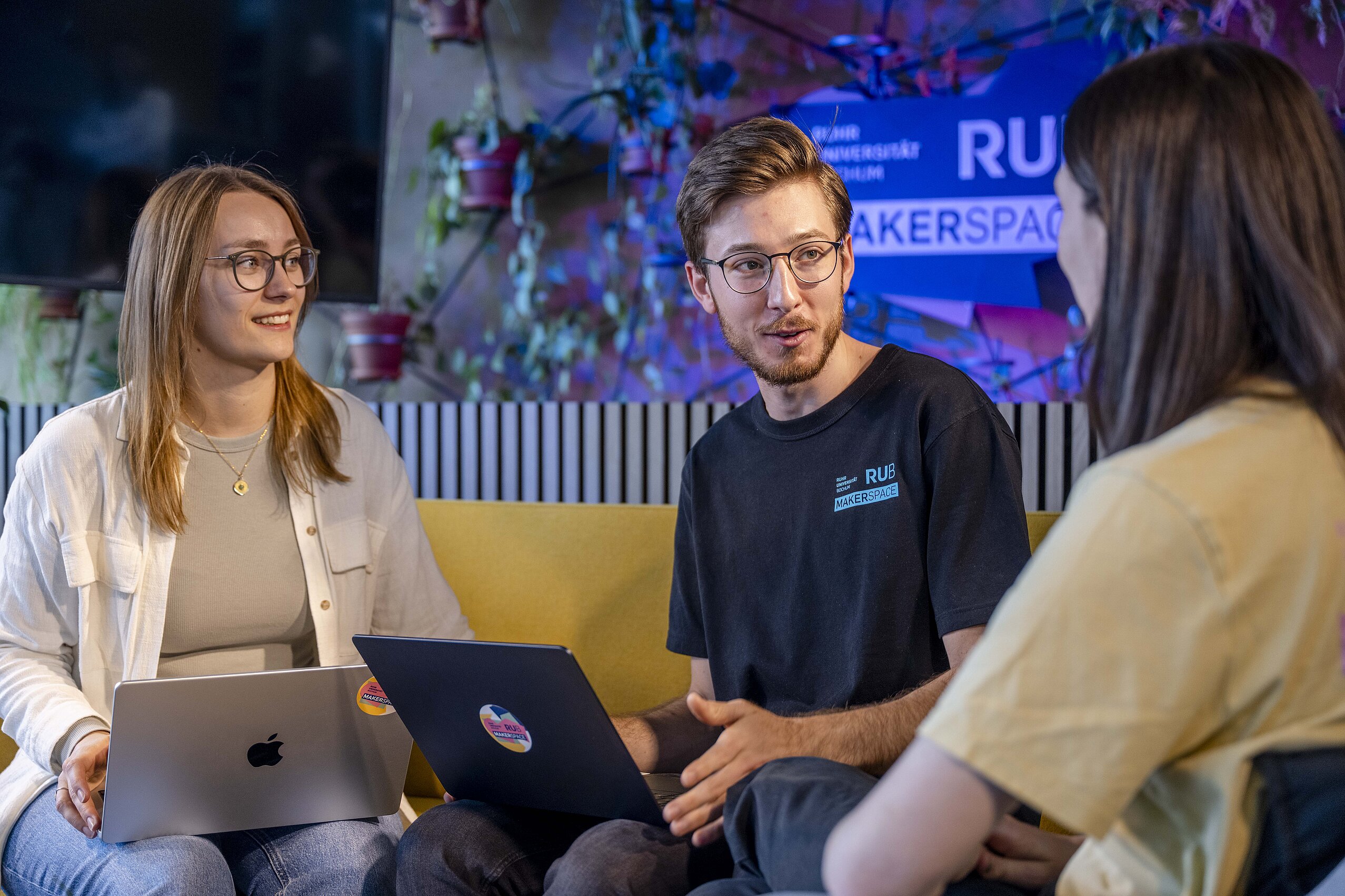 Drei Student:innen sitzen mit ihren Laptops auf der Couch und unterhalten sich