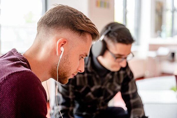 Zwei Studierende tragen Kopfhörer und arbeiten konzentriert.