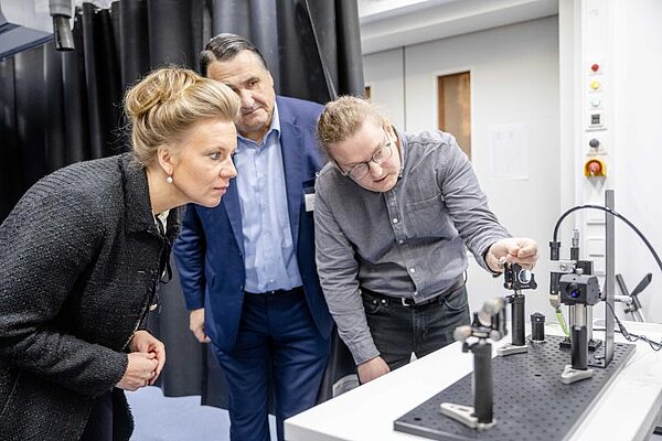   Claudius Hoberg (rechts) zeigt Ministerin Ina Brandes und Rektor Martin Paul einen Versuchsaufbau. 
