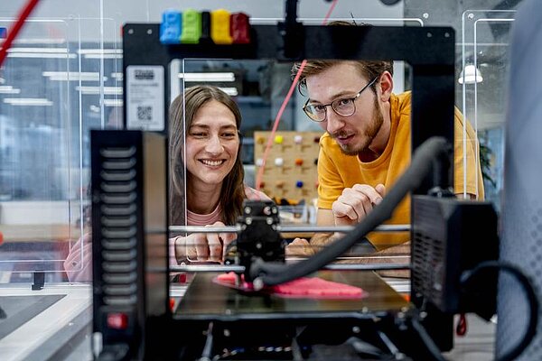 Zwei Personen betrachten einen 3D-Drucker beim Druck.