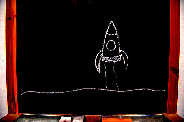 Mit Kreide aufgemalte Rakete auf einer schwarzen Tafel