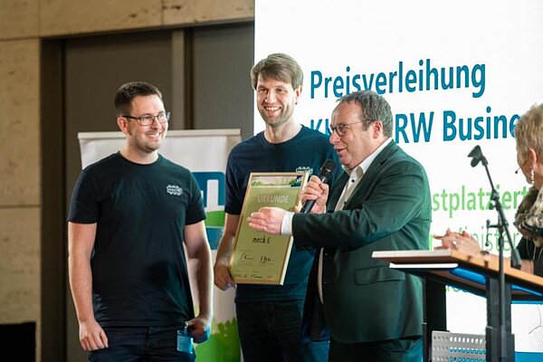 Umweltminister Oliver Krischer (rechts) gratuliert Philip Schmitt (links) und Steffen Wittemeier.