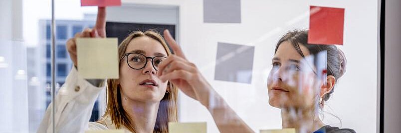 IDEA.Lab @ Worldfactory Zwei Personen kleben Notizzettel auf eine Glaswand