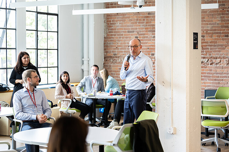 A man talking into a microphone in front of some students.