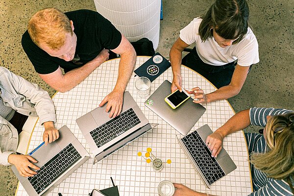 Gruppe junger Menschen sitzt an einem Tisch und arbeitet an Laptops.